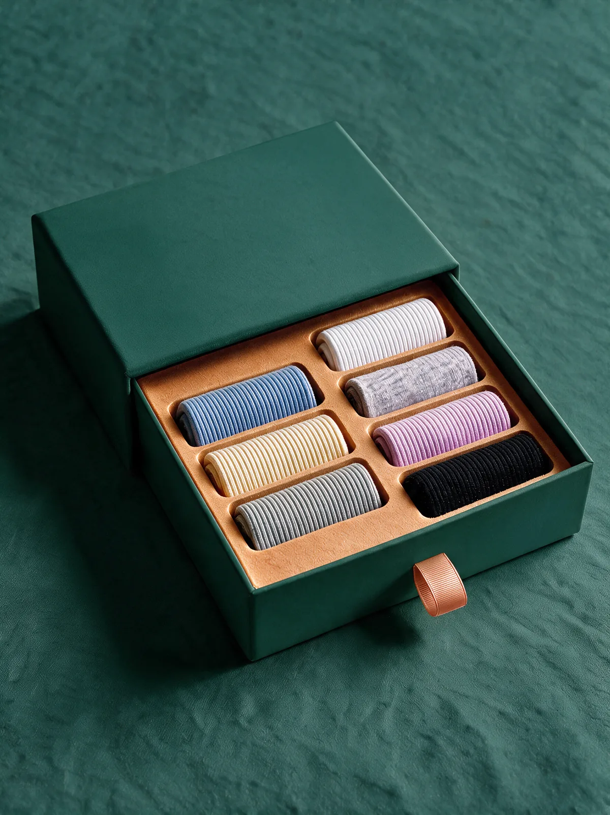 Deep pine drawer box slid open to reveal seven rolled pairs seated in a warm amber tray, copper ribbon pull at the front